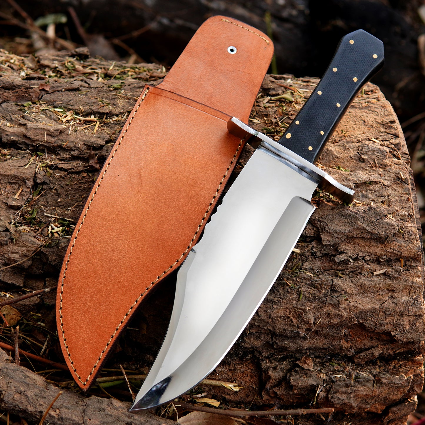 Handmade bowie style knife with polished steel blade, durable synthetic handle, and leather sheath displayed on wood.