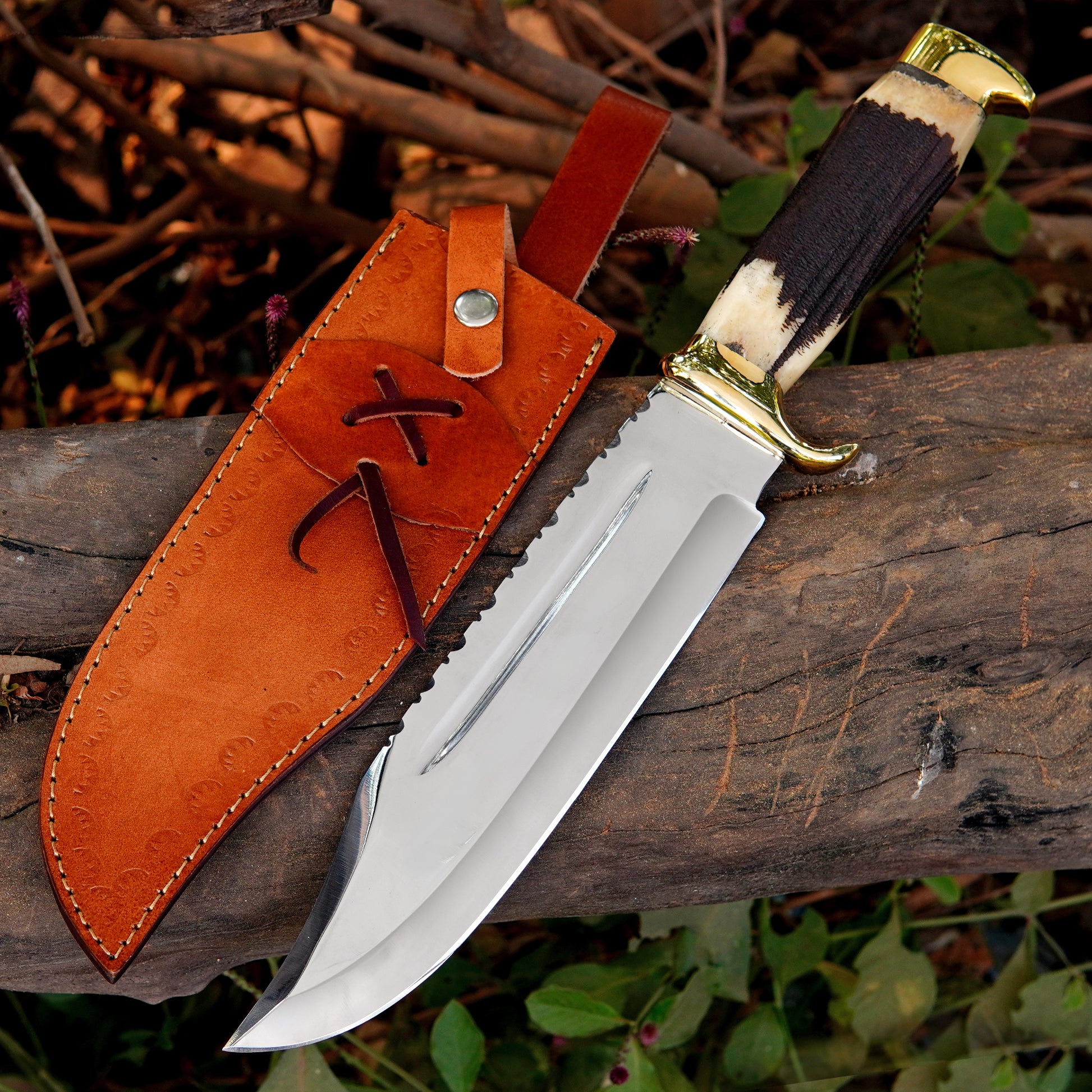 Handmade bowie style knife with polished steel blade, natural material handle, and leather sheath displayed on wood.