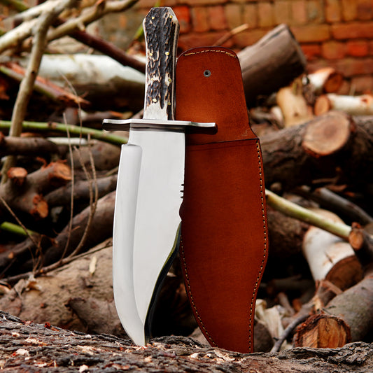Handmade bowie style knife with polished steel blade, natural material handle, and leather sheath displayed outdoors.
