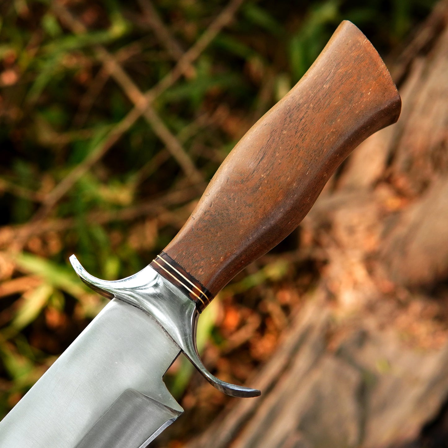 Outdoor lifestyle image of handcrafted camping knife resting on tree bark showing strong spine thick blade profile and balanced design for heavy duty cutting bushcraft and general wilderness use