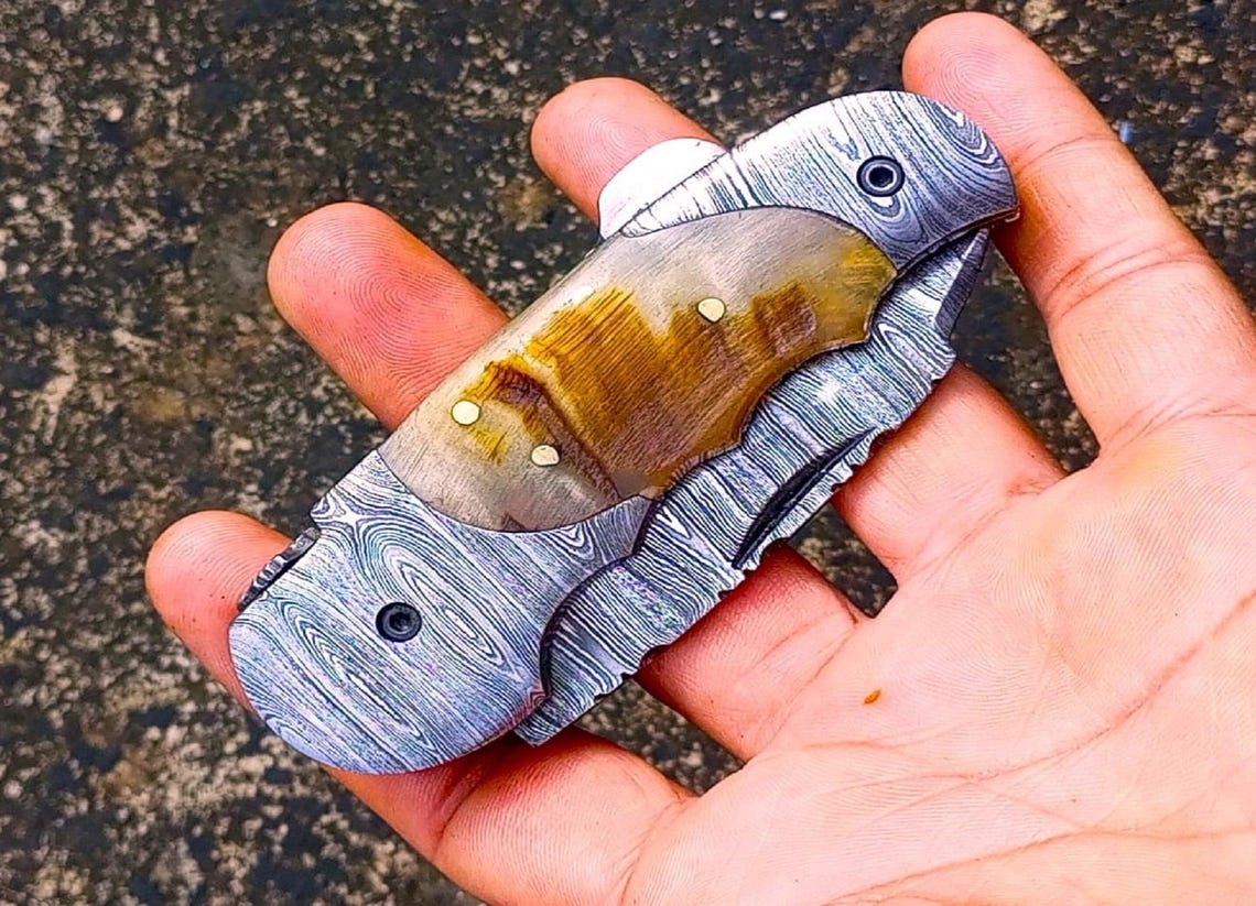 Close-up of Damascus pattern folding knife with brass liners and detailed spine file work.