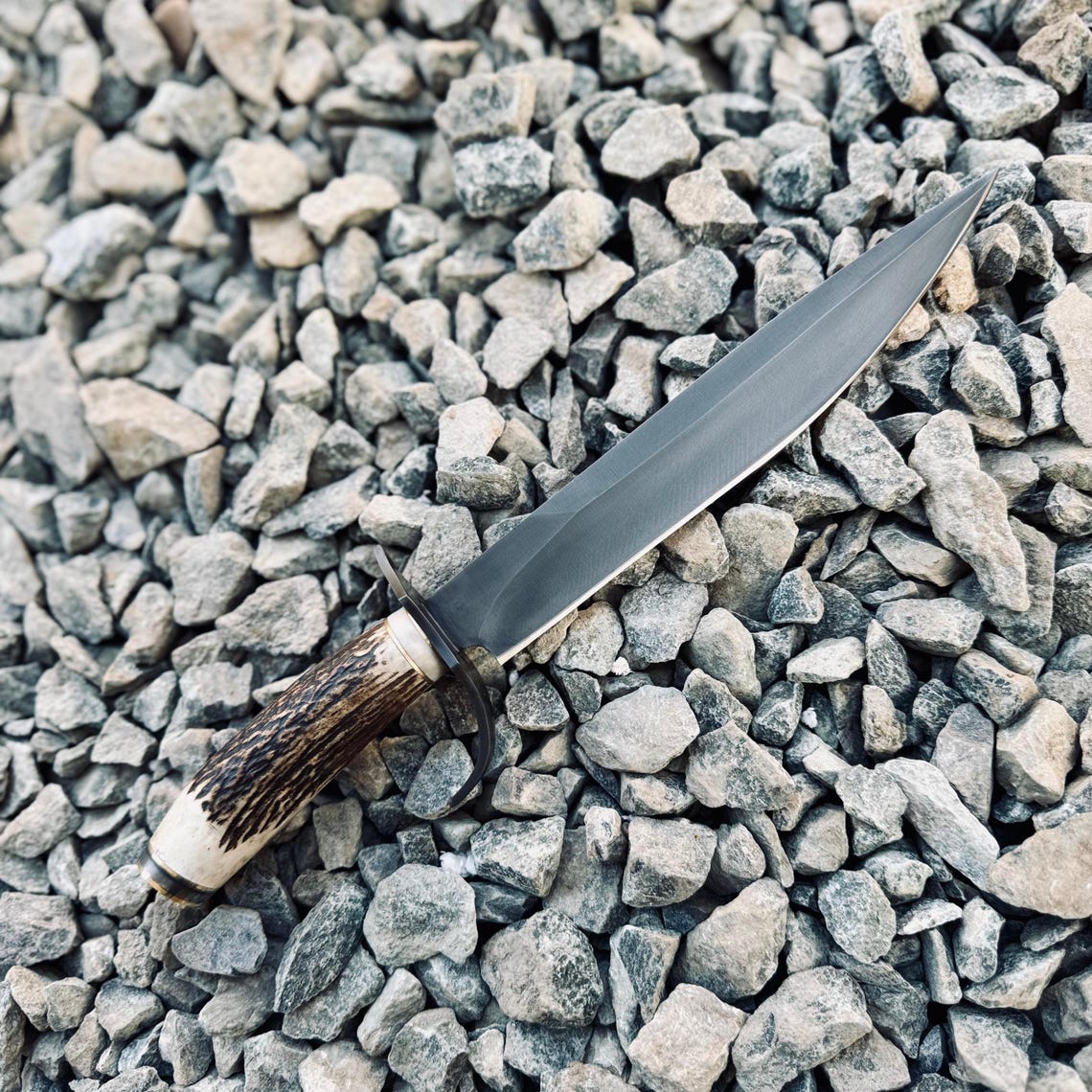 Handmade 5160 spring steel Bowie knife featuring a sharp satin-finished blade and a natural stag handle, perfectly balanced for strength and performance. Includes a custom black leather sheath, ideal for collectors, hunters, and outdoor adventurers who appreciate fine craftsmanship.