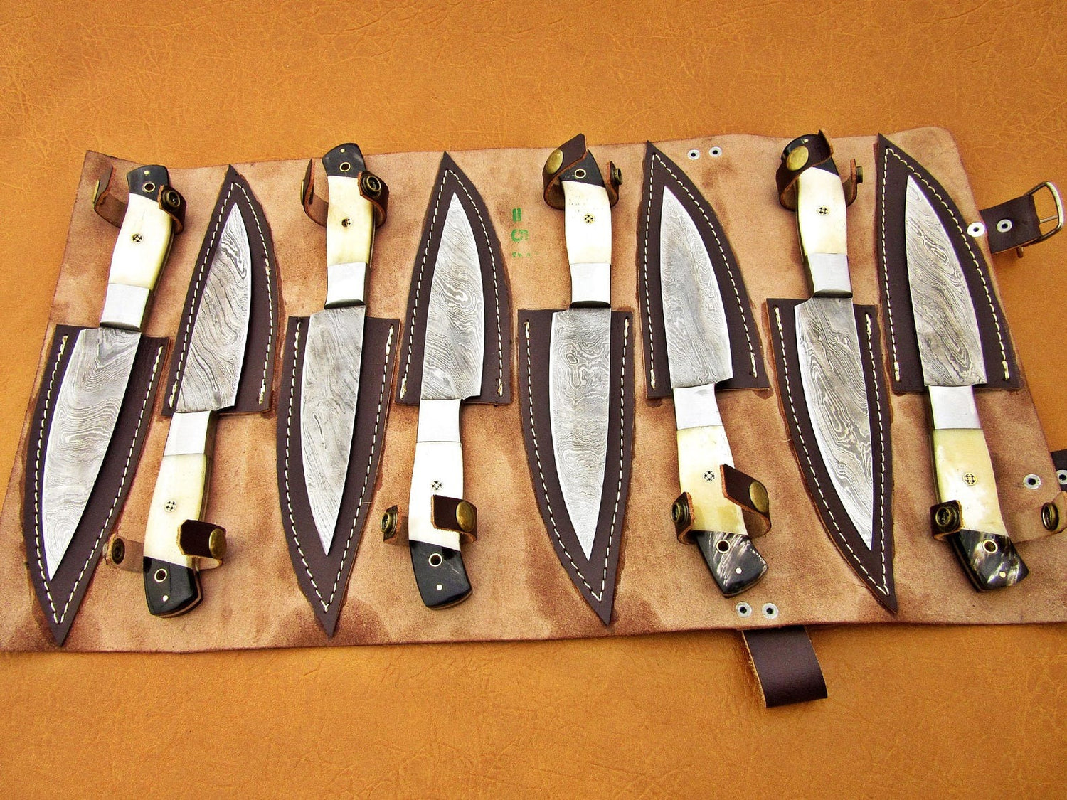 Unique white handle steak knife set with handmade Damascus steel blades displayed on leather background.