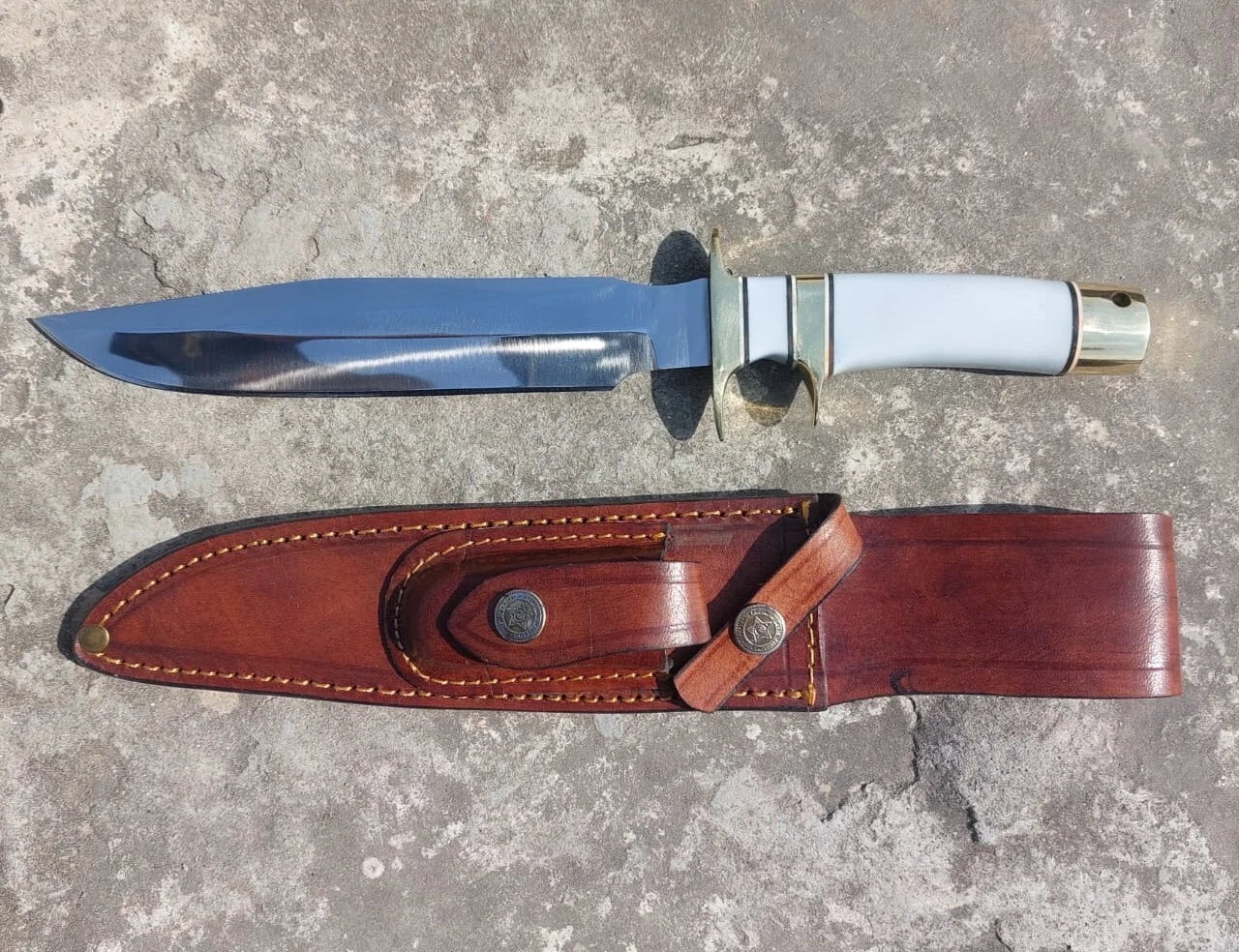 Outdoor and hunting knife with a white handle and polished blade, paired with a stitched leather sheath. Built with brass guard and pommel for balance and strength.