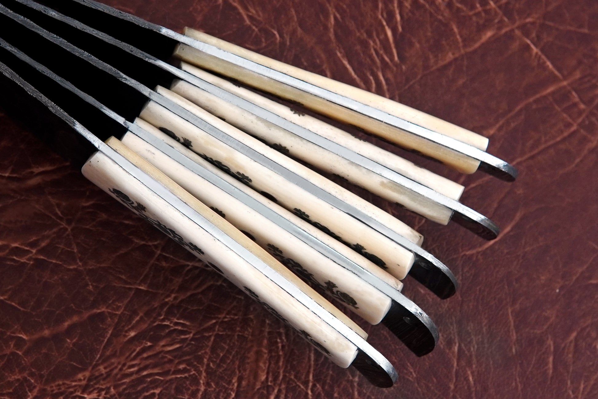 A kitchen knife set of 5 handmade Damascus steel blades with white natural material handles. Built with full tang durability, this chef set comes with a leather kit for storage. Engraving is free, making it a thoughtful gift.