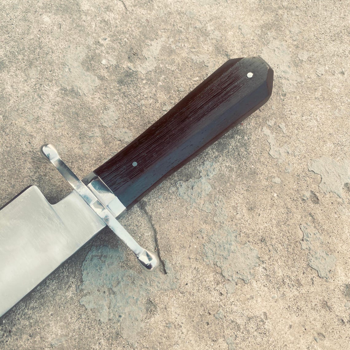 Close-up of dark wooden handle and polished cross guard of handmade Bowie knife.